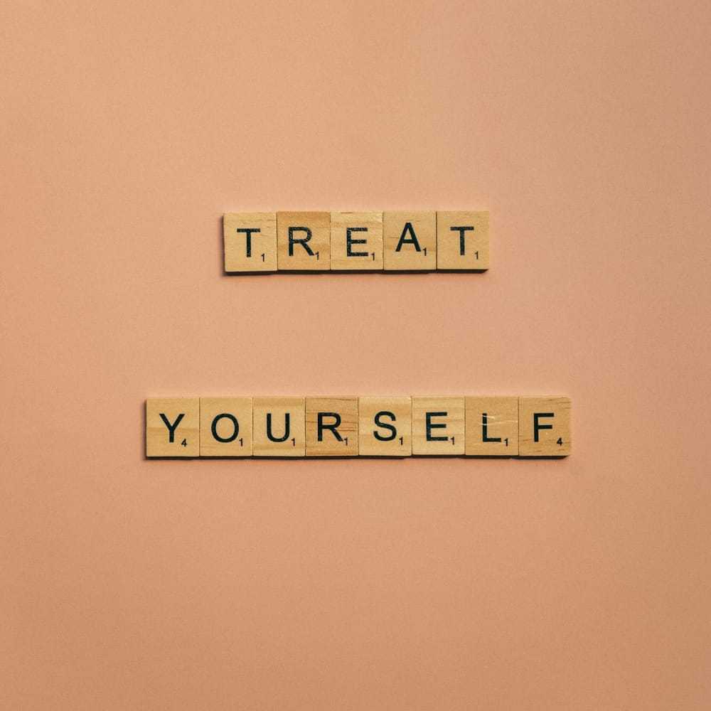 Scrabble tiles spell out "Treat Yourself" on a peach-colored background.