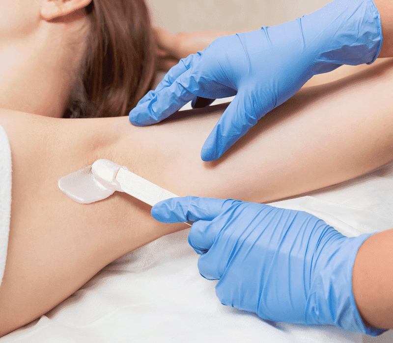 Person receiving a professional underarm waxing treatment by someone with blue gloves.