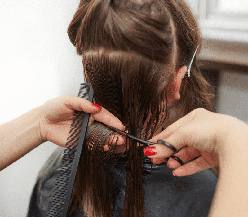 Person getting a haircut, close-up of hands trimming brown hair with scissors and a comb.