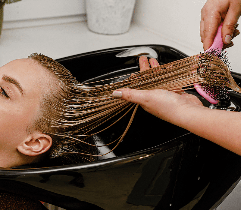 A person getting their hair washed and brushed at a salon sink.