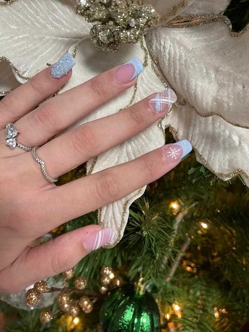 Hand with festive manicure in front of a Christmas tree, featuring French tips and holiday designs.