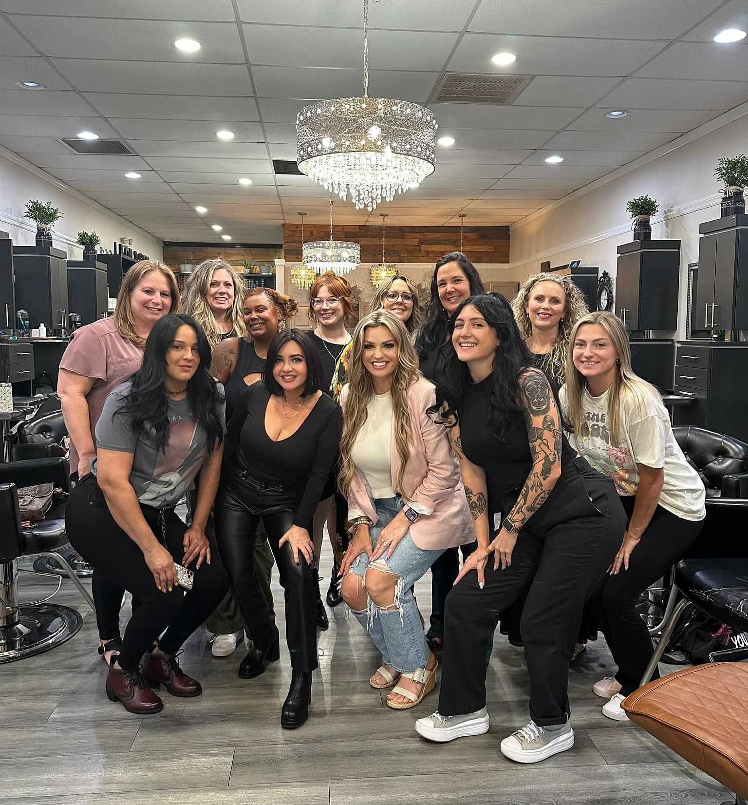 A group of smiling women posing together in a stylish, well-lit hair salon.